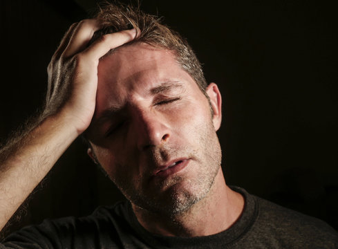 Young Attractive And Sad  Man Suffering Depression And Headache With Hand On His Tempo Head In Stress Looking Worried And Sick Isolated On Black