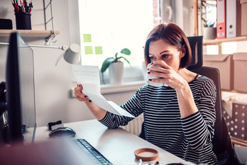 Woman reading mail at the office and drinking coffee