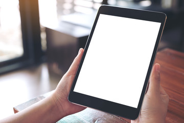 Mockup image of hands holding black tablet pc with blank white desktop screen on wooden table