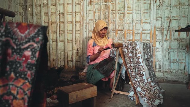 Adult indonesian woman painting batik with wax using canting in Pekalongan