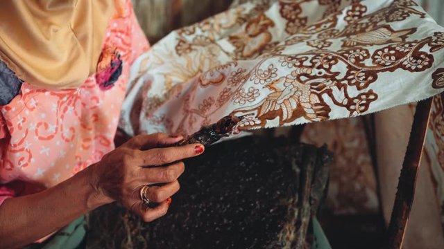 Close up of old indonesian woman hand painting batik with wax using canting in Pekalongan