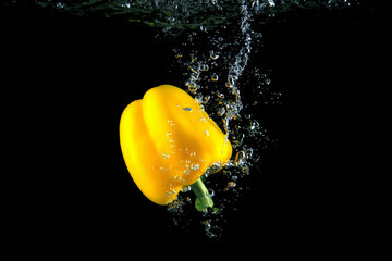 Yellow pepper and bright water splash. Healthy and tasty food on black background.