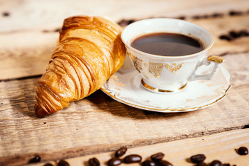 cup of delicious and fragrant coffee with a tasty croissant on a wooden table