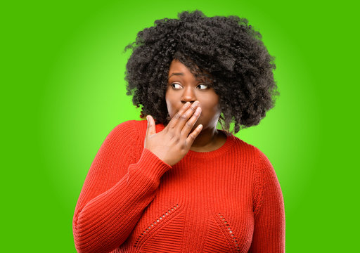 Beautiful african woman covers mouth in shock, looks shy, expressing silence and mistake concepts, scared