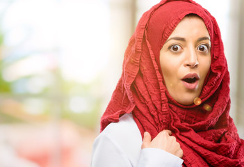 Young arab woman wearing hijab happy and surprised cheering expressing wow gesture, pointing with finger