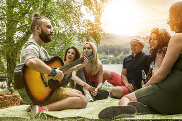 junge studenten singen und musizieren beim picknick am see und genießen unbekümmert ihre freizeit
