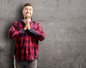 Young handsome man with hands together in praying gesture, expressing hope and please concept