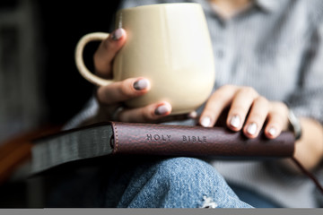 Young woman reading a book and holding cup of tea or coffee.