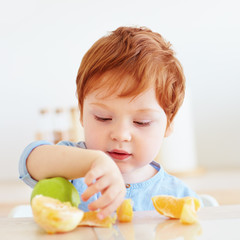 cute redhead toddler baby trying fresh apple and orange fruits