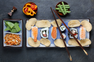 Arrangement of sushi with chopsticks, pickled vegetables and peppers on slate background