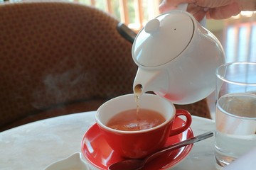 Side view of pouring tea with white tea pot and red tea cup in the time of tea break. Food and drink concept.