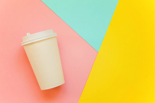 Paper coffee cup on blue, yellow and pink pastel colorful paper geometric flat lay background. Takeaway drink container. Template of drink cup for your design for put text, image, and logo mockup
