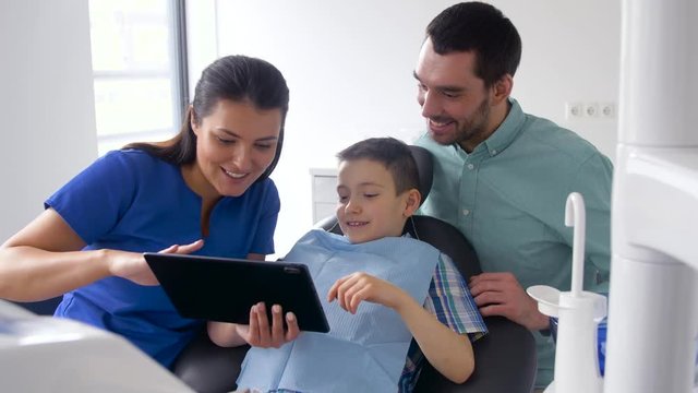 medicine, dentistry and healthcare concept - dentist showing tablet pc computer to father and son at dental clinic