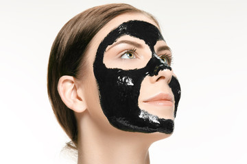 Young beautiful woman applying a mask for the face of the therapeutic black mud. Spa treatment