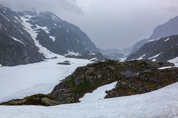 Frozen mountain river on the Norwegian Scenic Route Ryfylke in overcast cool day in summer time, Norway. Snow in mountains does not thaw even in the summer.