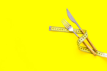 Diet, weight loss, slimming concept. Fork and knife with wound measuring tape on yellow background top view space for text