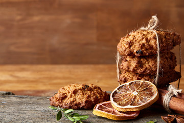 Christmas composition with chocolate biscuits, cinnamon and dried oranges on wooden background, close-up.