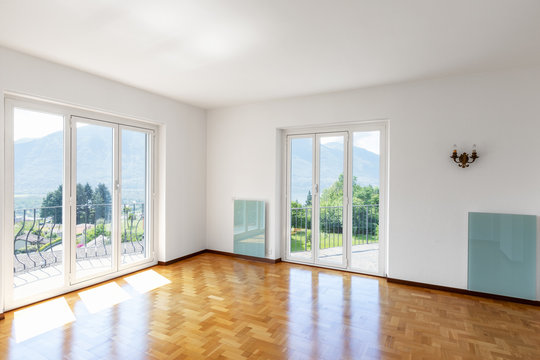 Empty white room with hardwood floors and large windows overlooking the Swiss hills
