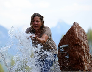 Abkühlung gefällig? Frau spritz im Freien mit Wasser am Brunnen