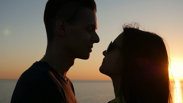 Profile of an amorous couple looking at each other and smiling happily at a picturesque sunset on the Black Sea shore in summer. 