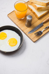 Eating in the process, fried eggs in a frying pan, toast  and orange juice for breakfast on a white background. Daylight.