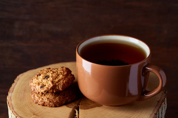 Cup of tea and cookies on a log over country style wooden background, close-up, selective focus
