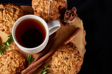 Christmas concept with a cup of hot tea, cookies and decorations on a log over wooden background, selective focus