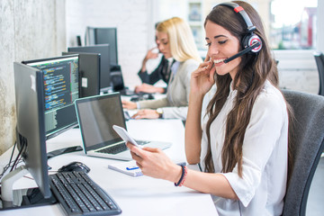 Smiling young woman with headset using phone in office
