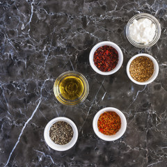 Bright spices in ceramic and glass bowls on a marble table. Background layout with free text space. The concept of cooking. The view from the top.
