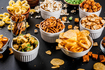 Variation different unhealthy snacks crackers, sweet salted popcorn, tortillas, nuts, straws, bretsels, back chalkboard copy space