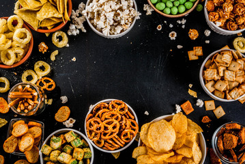Variation different unhealthy snacks crackers, sweet salted popcorn, tortillas, nuts, straws, bretsels, back chalkboard copy space