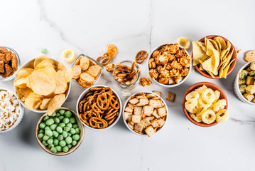 Variation different unhealthy snacks crackers, sweet salted popcorn, tortillas, nuts, straws, bretsels, white marble background copy space