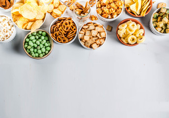 Variation different unhealthy snacks crackers, sweet salted popcorn, tortillas, nuts, straws, bretsels, white marble background copy space