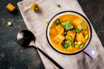 Homemade pureed carrot cream soup, with bread crackers, fresh herbs and cream. On a dark blue background,