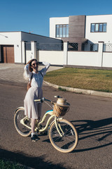 Naklejka na ściany i meble Pretty girl in hat and dress by cruiser bicycle in suburb