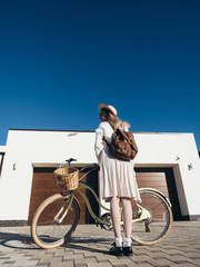 Fototapeta na wymiar Pretty girl in hat and dress by cruiser bicycle in suburb