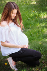 Young Caucasian woman at 9th month of pregnancy sits on green grass