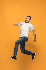 Fototapeta na wymiar Freedom in moving. handsome young man jumping against orange background