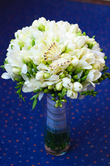 A wedding bouquet of white freesias with a decorative butterfly in vase on blue background.