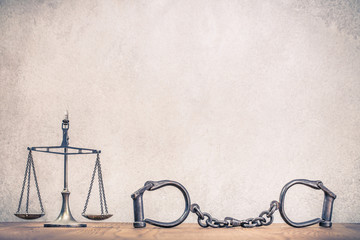 Vintage law scales and handcuffs on wooden table front textured concrete wall background. Symbols of justice conceptual still life. Retro old style filtered photo