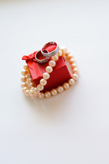 Wedding rings and a string of pearls on a red jewelry box on a white background.