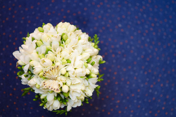 A wedding bouquet of white freesias with a decorative butterfly on blue background.