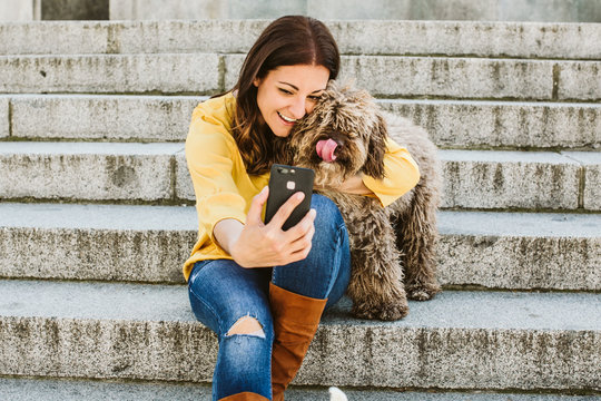 Young beautiful woman taking photograph of her sweet dog playfuly in a lovely park of the center of Madrid. Seated in stone stairs. Lifestyle