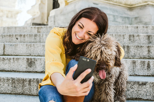 Young beautiful woman taking photograph of her sweet dog playfuly in a lovely park of the center of Madrid. Seated in stone stairs. Lifestyle