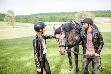 Young couple riders standing near the beautiful horse on the green meadow