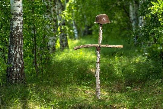 Helmet on the birch cross. The grave of an unknown German soldier in the forest. Imitation. WW2 recovery.