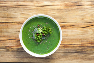Spinach green soup with broccoli in white bowl on wooden background top view.