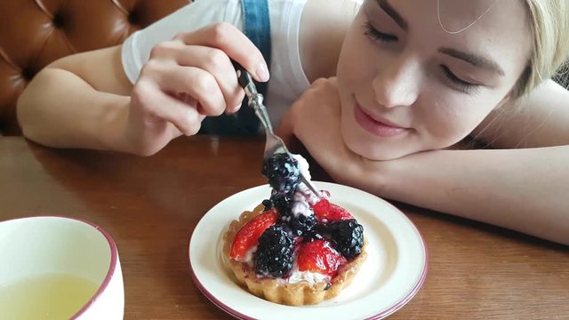 Young blond Woman Eating the blackberry Cake in cafe