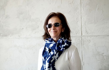 Middle aged woman smiling with sun glasses on concrete background.