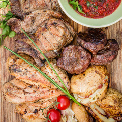 Set of grilled meat - chicken breast, steaks on bone, steak chateaubriand, cherry tomatoes, sauce and baked potato. barbecue..and grill, top view